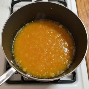 Caramelizing sugar in a saucepan on a stovetop, showing the golden liquid forming during the process.