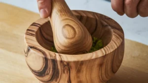 Seasoned meat mixture in a bowl with crushed celery in a wooden mortar.