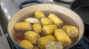 Corn on the cob and garlic boiling in a large pot of water.