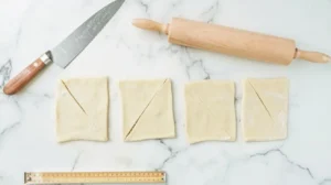 Cutting dough into triangles for Gipfeli recipe, with a rolling pin and knife nearby.