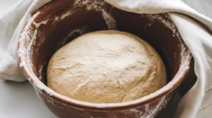 Dough rising in a bowl, covered with a cloth, ready for the next step in a Gipfeli recipe.