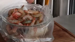 Raw shrimp in a clear glass bowl lined with a plastic cooking bag.