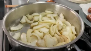 Sliced onions sautéing in a pan with oil.