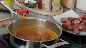 Pan filled with seasoned butter sauce next to sliced smoked sausage.