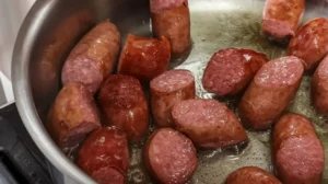 Sliced smoked sausage browning in a pan with oil.