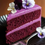 Purple velvet cake with smooth frosting, topped with edible flowers in shades of white, lavender, and violet